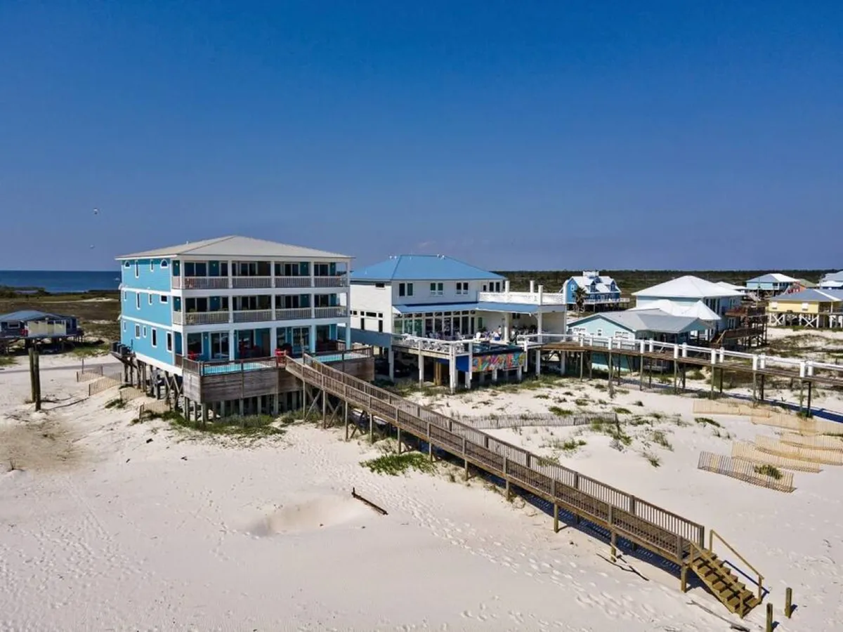 Colorful beach houses line a path leading through sand dunes to the beach. The scene captures the inviting, playful atmosphere of the Fort Morgan area and offers a glimpse of the coastal lifestyle and outdoor adventures available nearby.