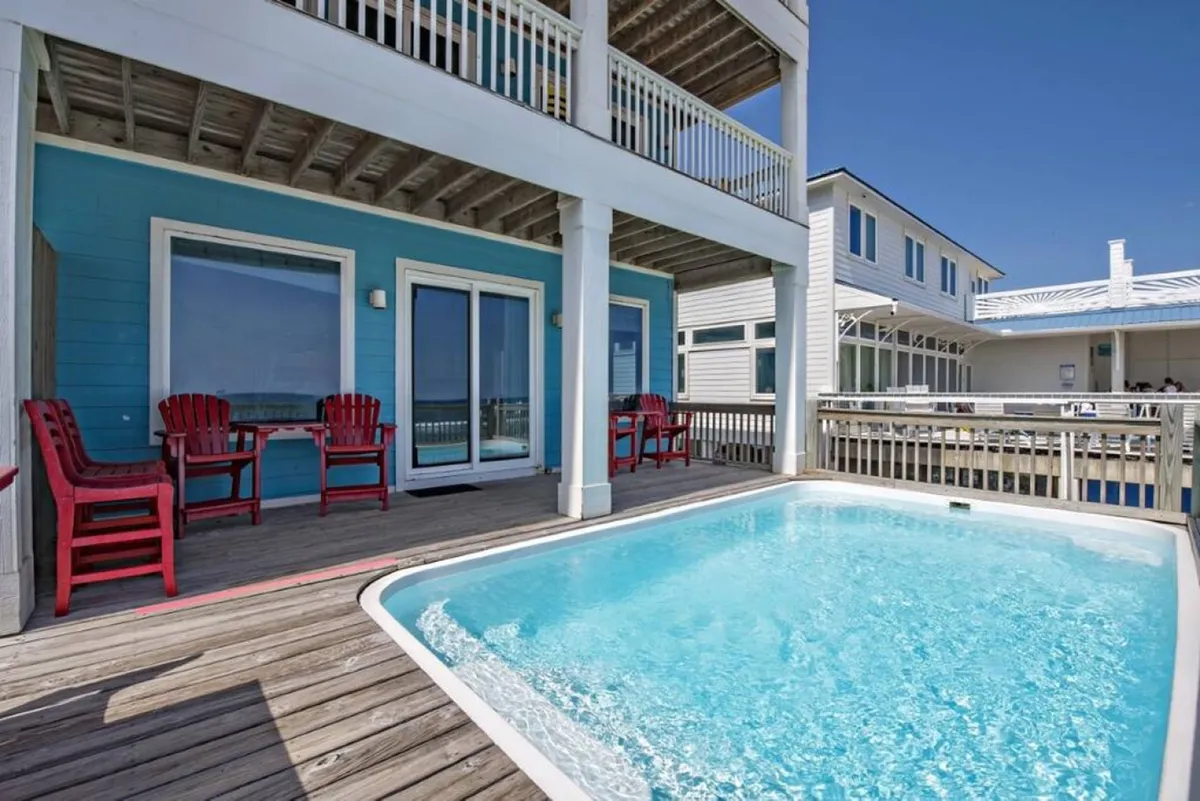 A vibrant pool area featuring a swimming pool surrounded by red chairs and a blue wall, bathed in sunlight. The scene captures a lively outdoor space perfect for swimming, sunbathing, and socializing with friends.