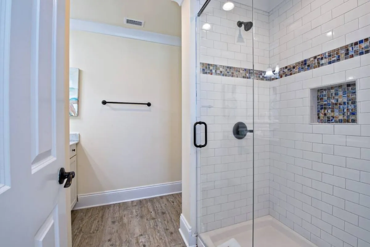 A bright, spa-like private bathroom featuring a glass shower enclosure, colorful accent tile, and a sleek vanity area. The space is clean, modern, and inviting, reflecting a tranquil atmosphere for relaxation and self-care.