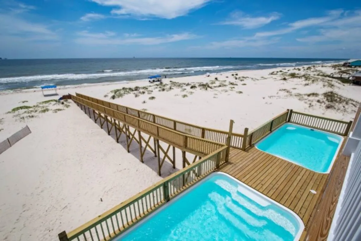 A tranquil scene with two hot tubs on a wooden walkway overlooking the ocean, inviting guests to relax under open skies. The setting feels secluded and serene, ideal for both quiet reflection and social gatherings after a day of celebration.