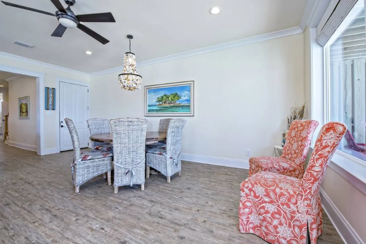A welcoming dining area featuring a woven dining set, colorful accent chairs, and a chandelier, surrounded by framed artwork. The layout is ideal for family meals, celebrations, and memorable gatherings, highlighting the home's ability to flexibly accommodate various group sizes and occasions.