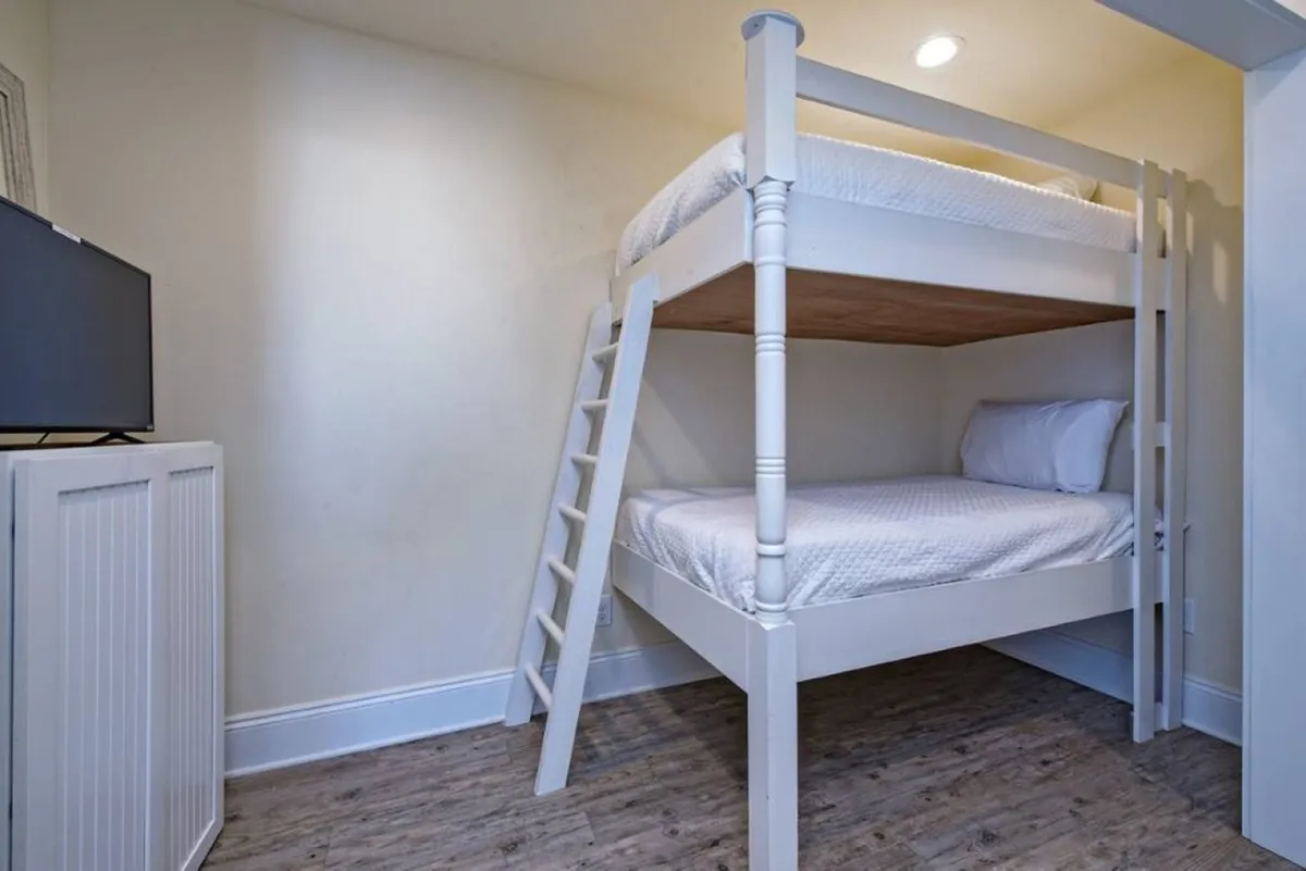 A playful and cozy bunk room with a built-in bunk bed featuring soft bedding, a television mounted on the wall, and a sturdy ladder for easy access. The atmosphere is inviting, ideal for kids or teens, with space for sleepovers and movie nights.