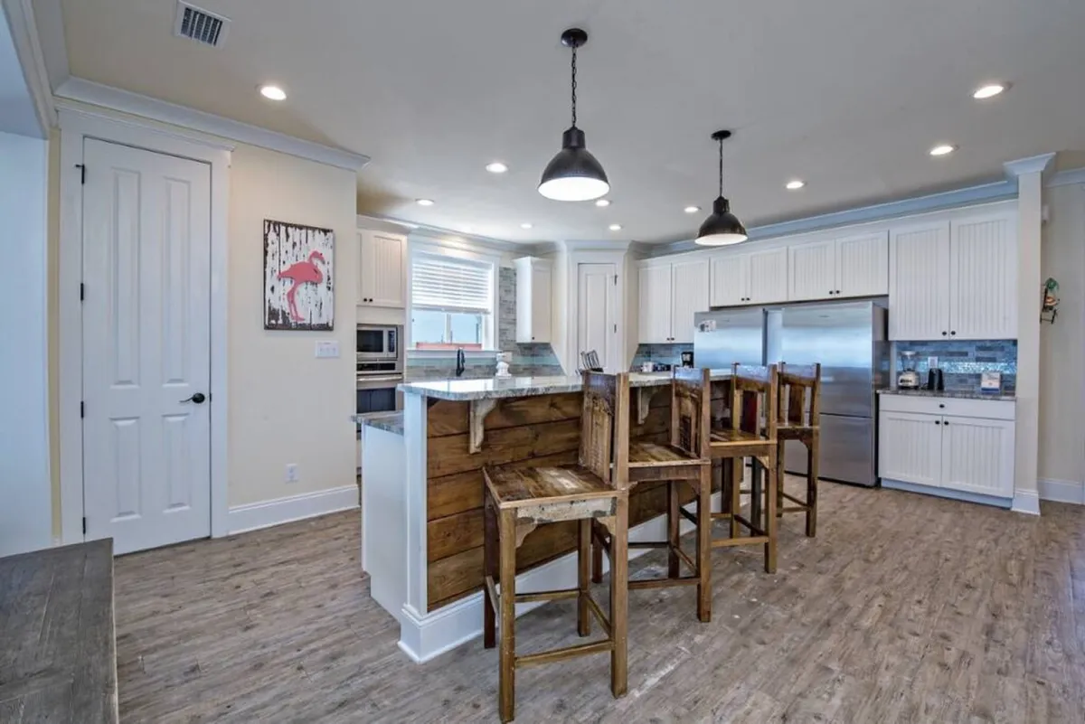 A modern, chef-inspired kitchen with a large island, bar stools, stainless steel appliances, and warm wooden accents. The space is filled with natural light, making it ideal for cooking, entertaining, and family feasts.
